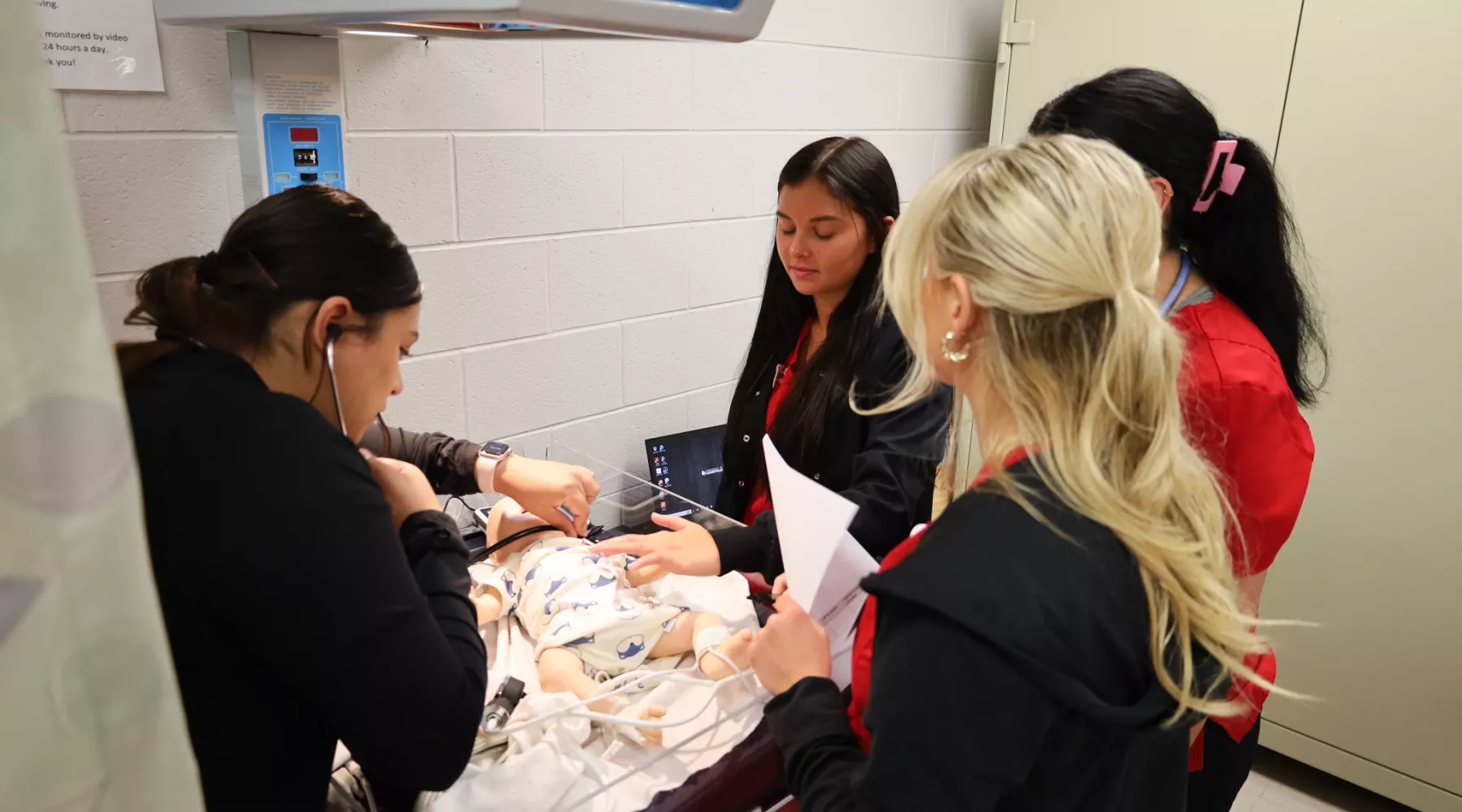 BSN students performing clinical simulation with infant manikin.