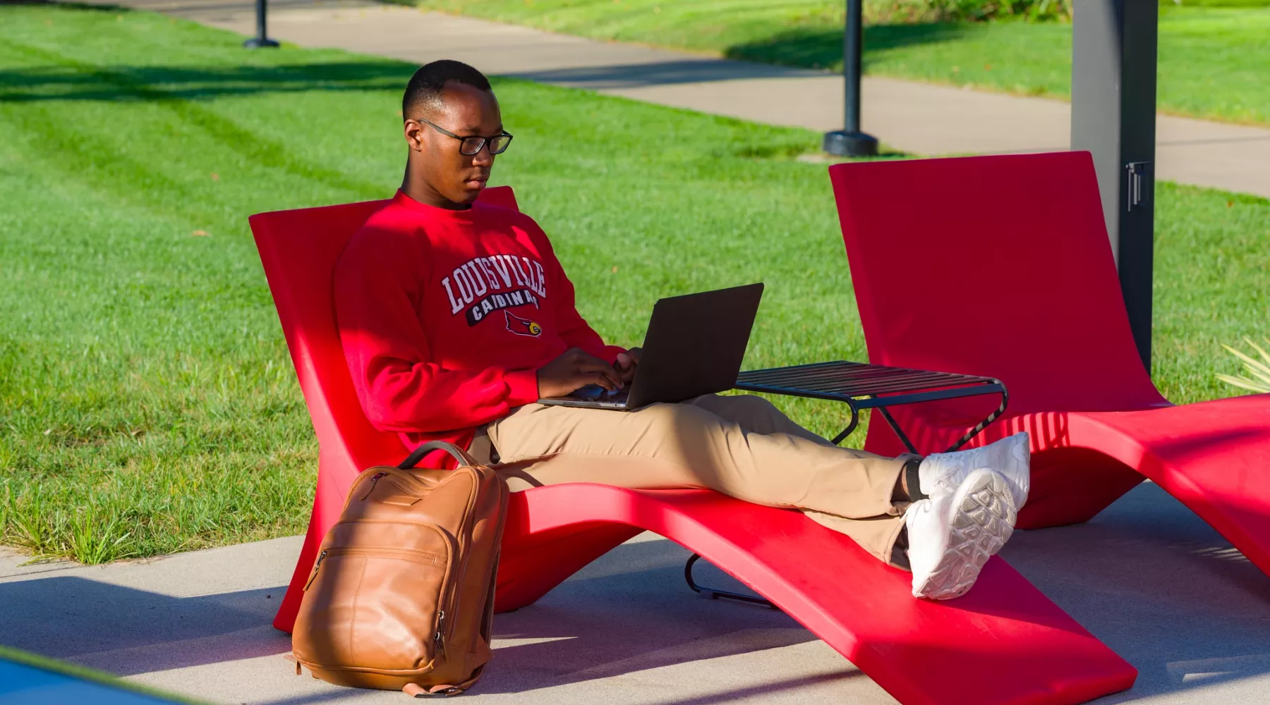 A student lounges in a chair in the 2020 Pavilion using a laptop