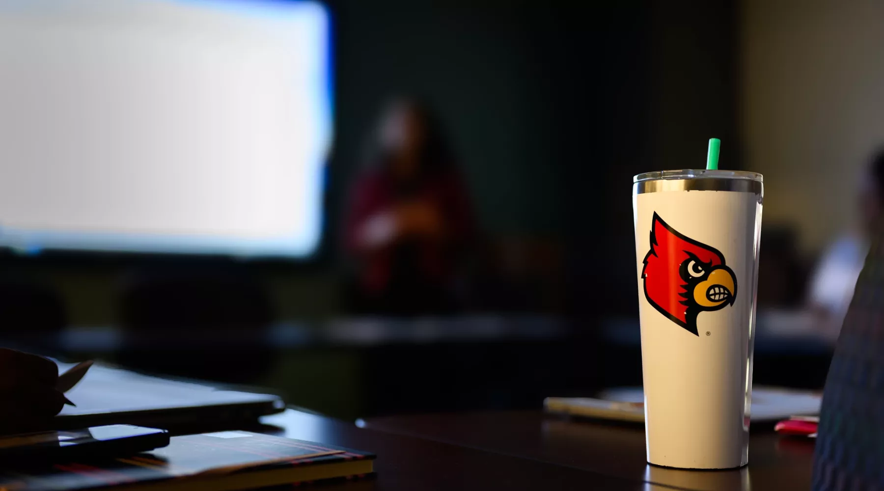 Close-up of a cup with the Cardinal Bird on it in a dark room where a presentation is being given in a classroom
