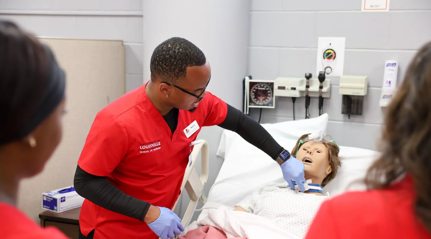 University of Louisville School of Nursing student in the simulation lab with gloves on and preparing to practice on a…