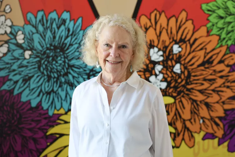 University of Louisville School of Nursing alumnus, Patricia Howard, standing in front of a multicolored, floral mural.