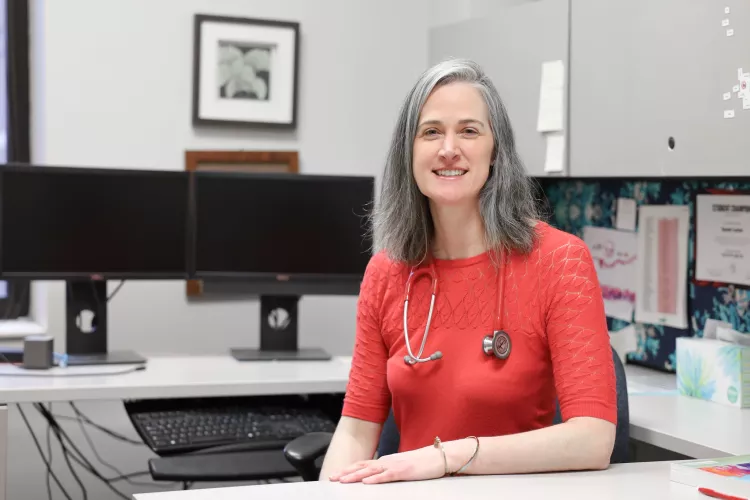 University of Louisville School of Nursing Professor and Kentucky Health Racing Services Center practitioner, Sarah Carter in the School of Nursing. Sarah sits in her office with a stethoscope around her neck.
