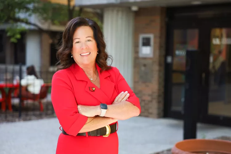 University of Louisville School of Nursing Dean, Dr. Whitney Nash. Nash stands in front of the School of Nursing on HSC campus in a red dress with a cardinal head pin.