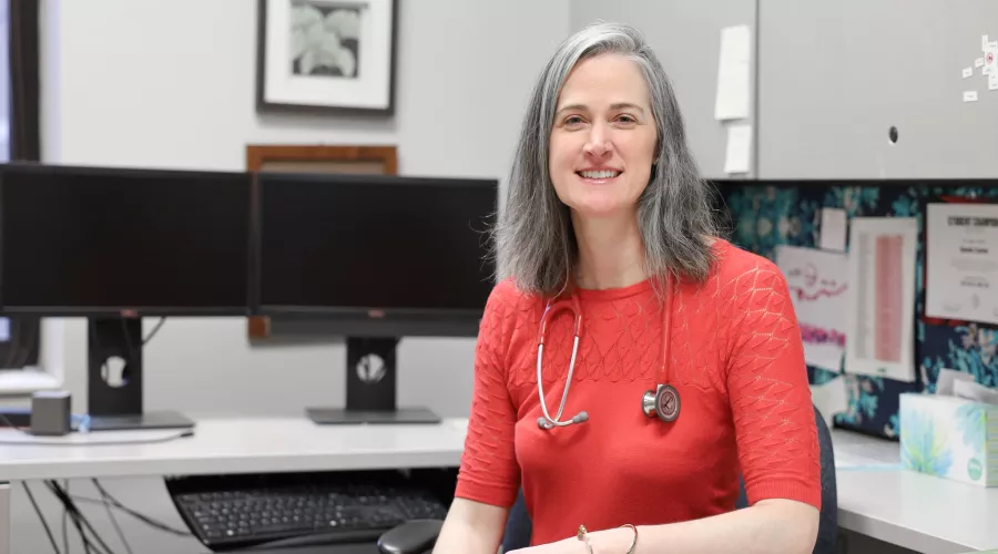 University of Louisville School of Nursing Professor and Kentucky Health Racing Services Center practitioner, Sarah Carter in the School of Nursing. Sarah sits in her office with a stethoscope around her neck.