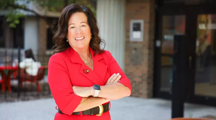 University of Louisville School of Nursing Dean, Dr. Whitney Nash. Nash stands in front of the School of Nursing on HSC campus in a red dress with a cardinal head pin.
